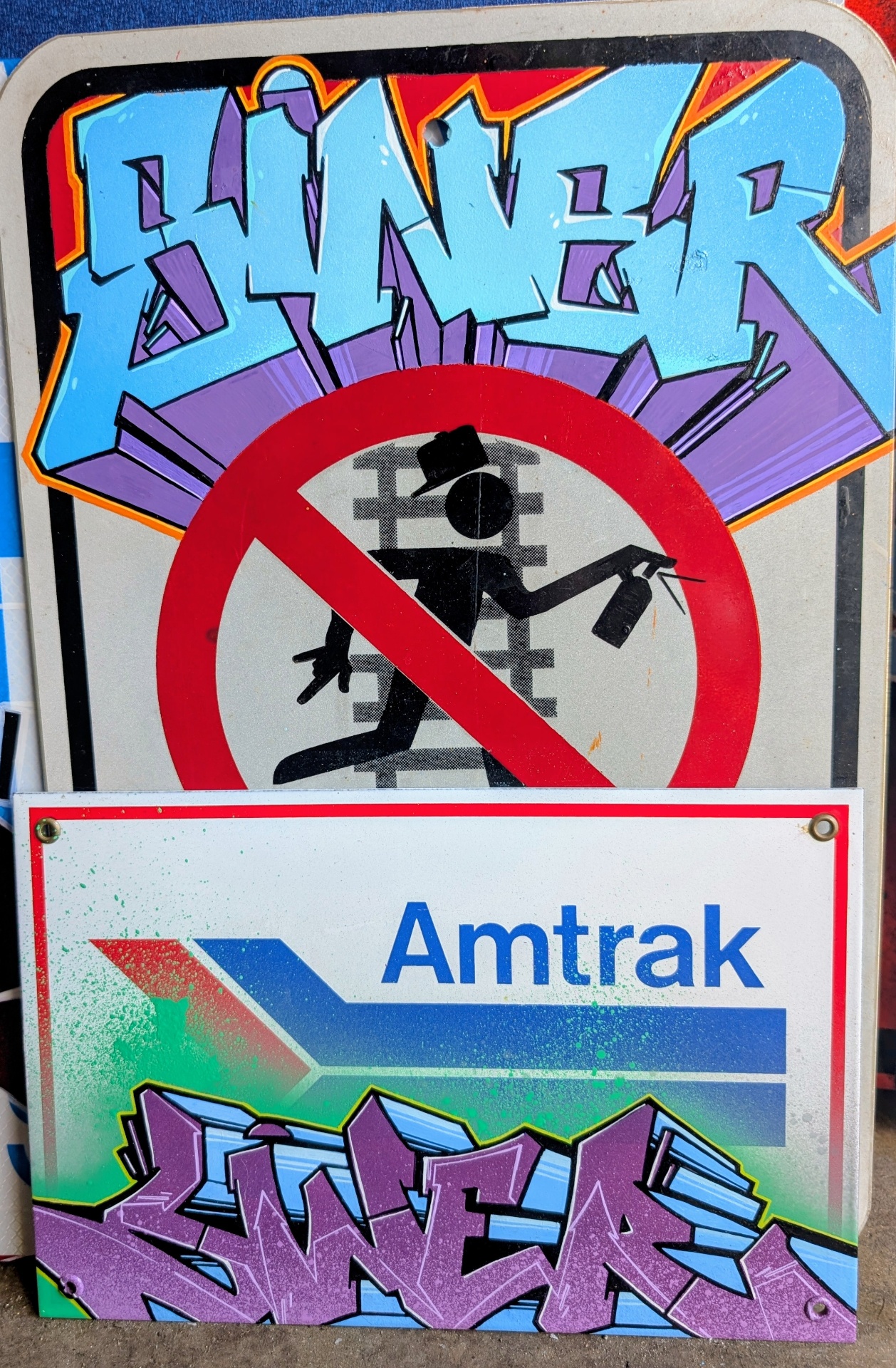 Stacked no-graffiti and Amtrak signs painted with blue and purple SINER wildstyle
